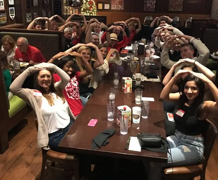Members spelling O-H-I-O with their arms along a long table